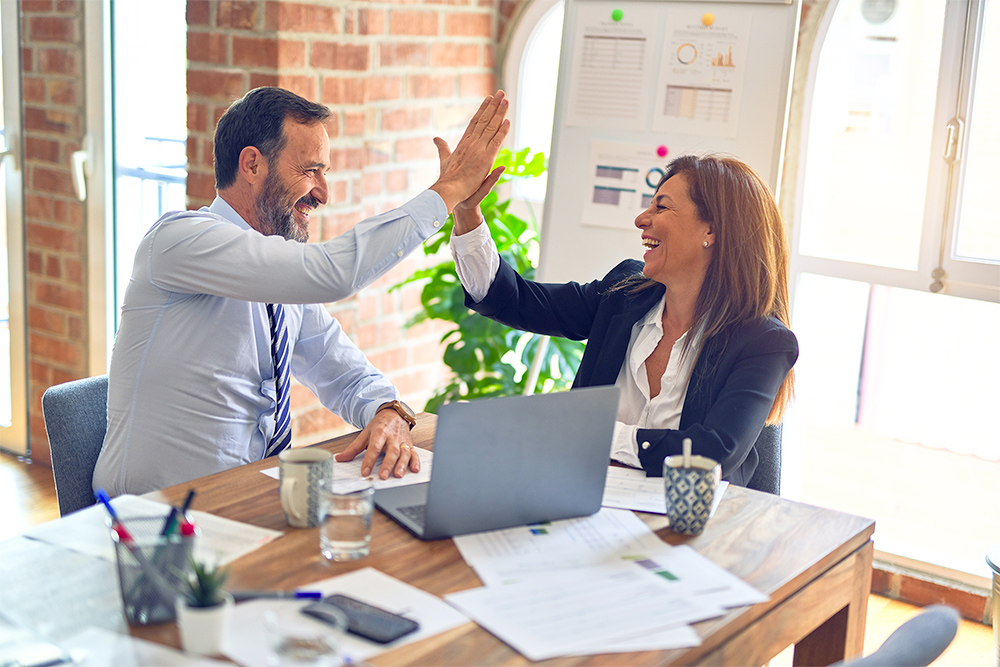 Man and woman doing a high-five over a laptop on a desk