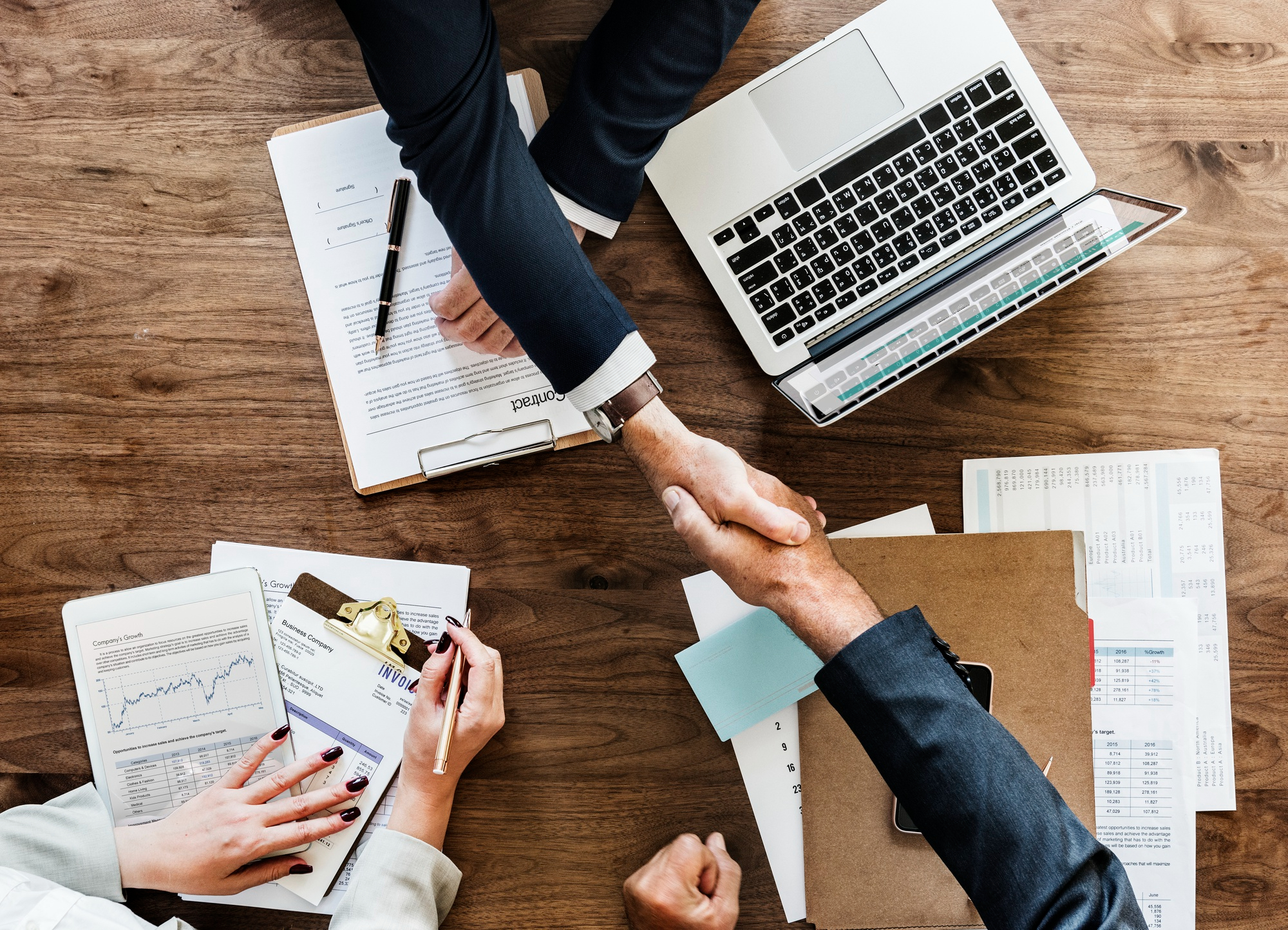 Birdseye view of two people shaking hands above paperwork and laptops on a table